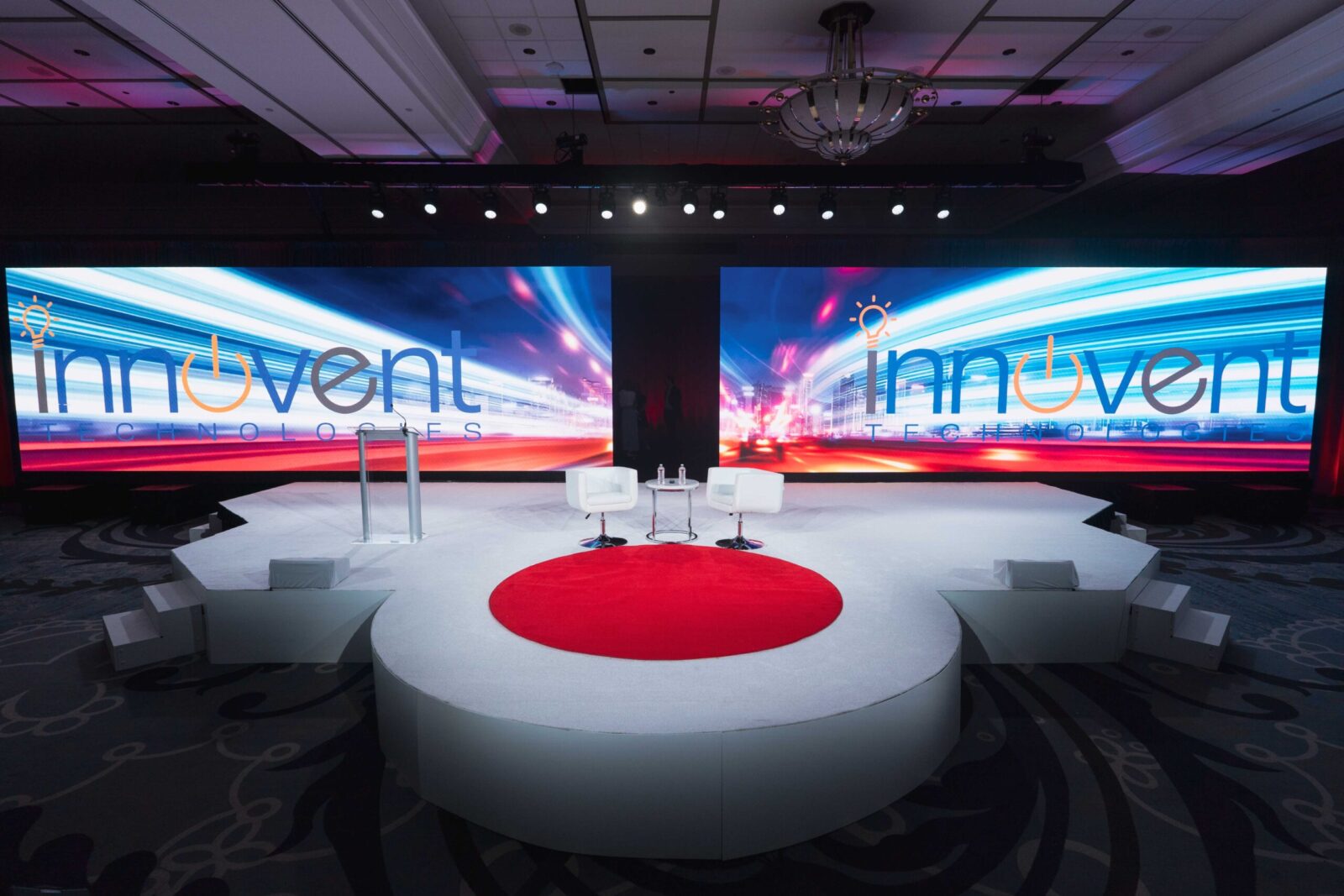 Innovent Technologies corporate event stage design at Cobb Galleria with dual LED walls, circular white platform, red center accent, podium, and lounge seating