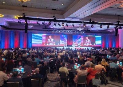 Large corporate conference ballroom with full audience seating, dual LED video walls, stage lighting truss, and live panel discussion produced by Innovent Technologies