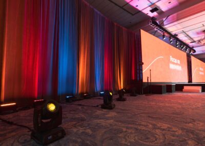 Corporate event stage with large LED video wall, red and blue drape uplighting, and professional stage lighting fixtures in ballroom setting