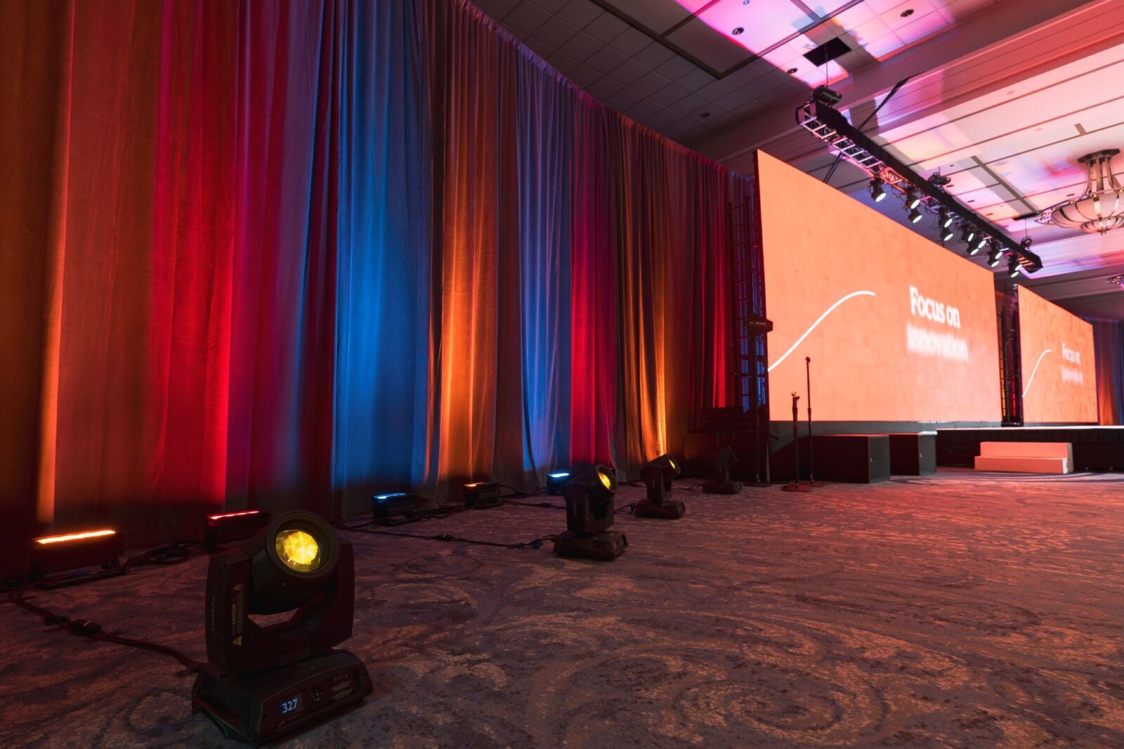 Corporate event stage with large LED video wall, red and blue drape uplighting, and professional stage lighting fixtures in ballroom setting