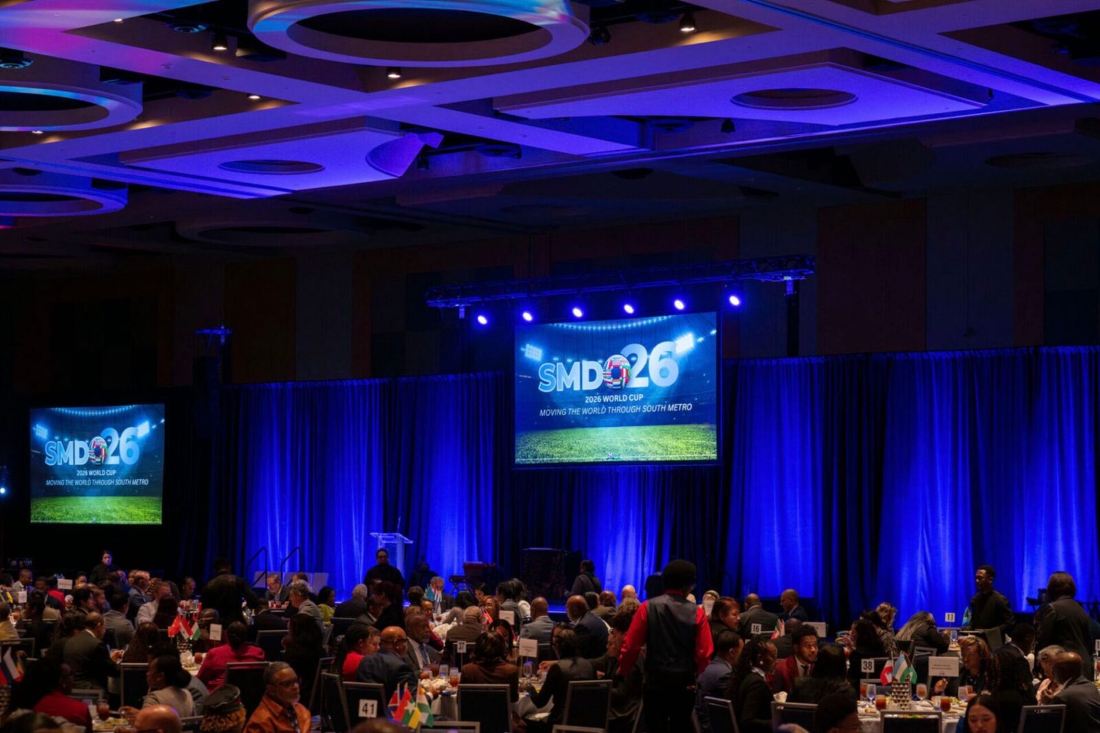 SMDO 2026 Outlook Conference luncheon program with large-format screen and blue stage lighting