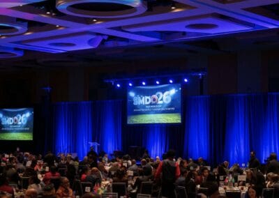 SMDO 2026 Outlook Conference luncheon program with large-format screen and blue stage lighting