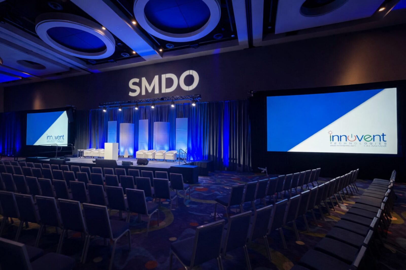 SMDO 2026 conference stage setup with seating, dual projection screens, and blue lighting design by Innovent Technologies