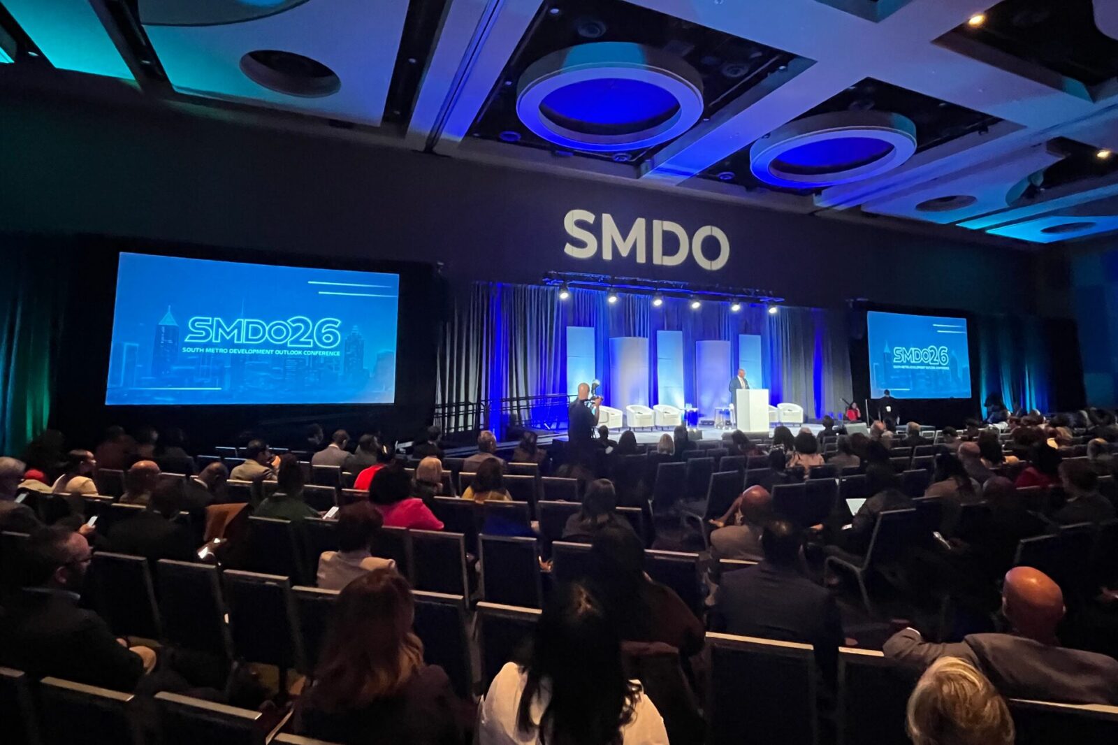 SMDO 2026 Outlook Conference luncheon program with large-format screen and blue stage lighting