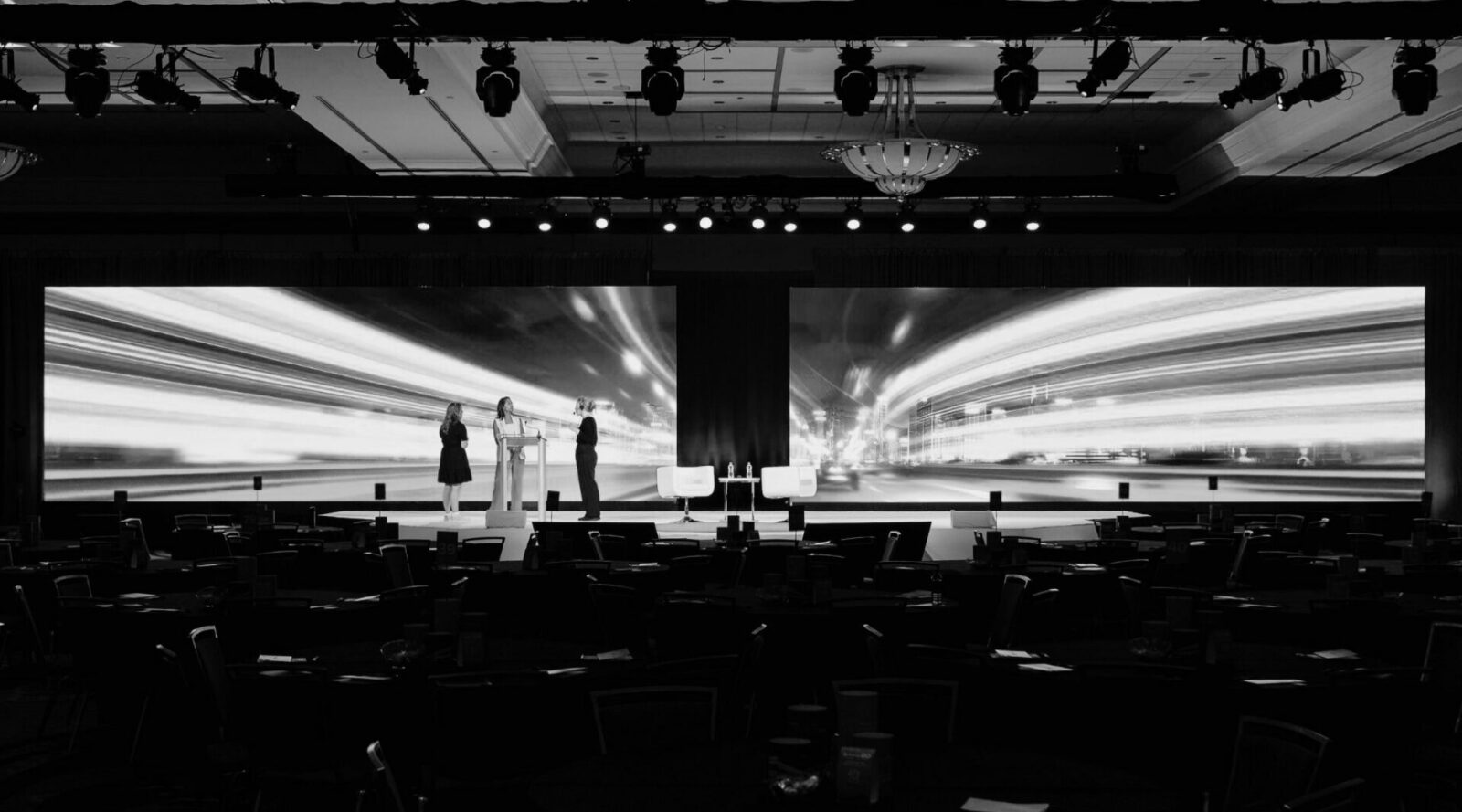 Conference stage with large LED video walls displaying high-resolution content compared to traditional projection screens in a corporate event setting