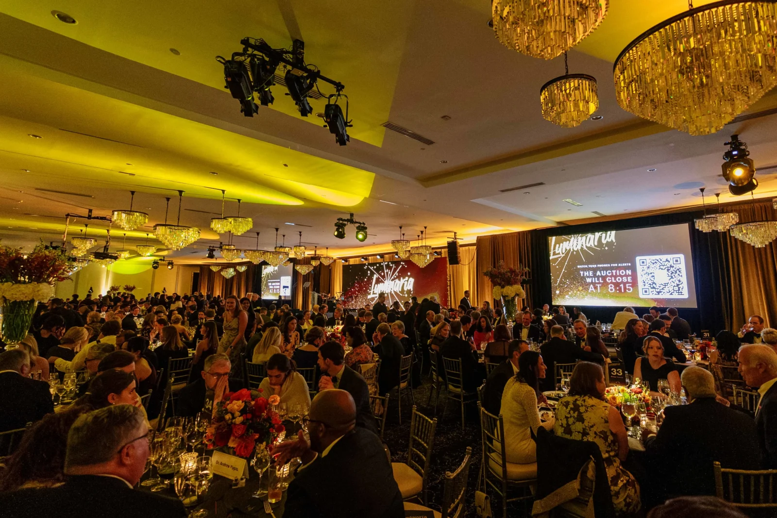 Large corporate event featuring presentation screens, audience engagement technology, stage lighting, and audiovisual production in a ballroom setting.