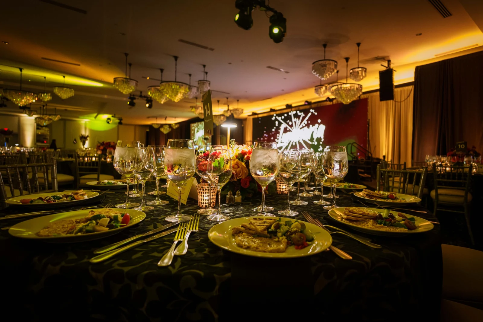 Elegant gala ballroom with warm architectural lighting, banquet tables, and a large LED video display behind the stage.